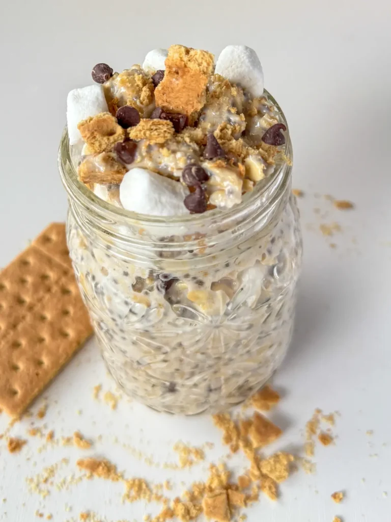 A fully loaded s'mores overnight oats on a counter next to a graham cracker.