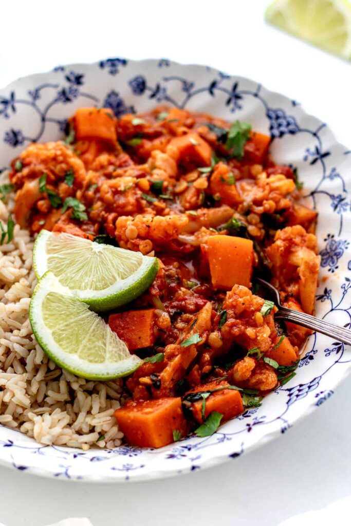 A bowl of red curry lentils with sweet potatoes, spinach and rice in a decorative bowl.