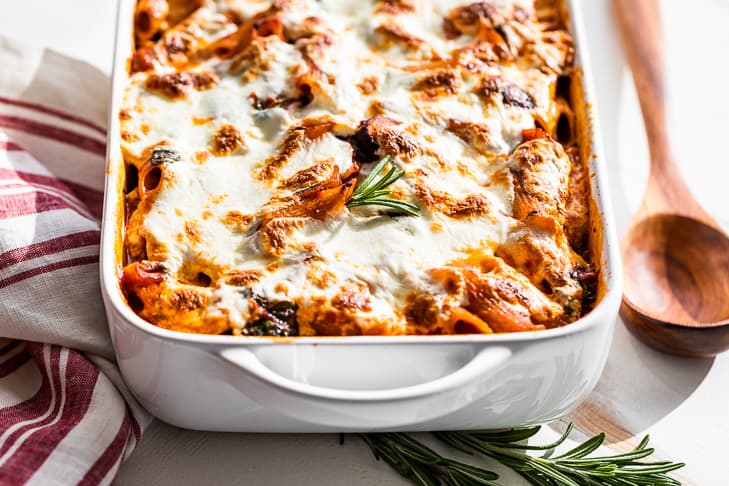 A cheesy vegetarian pasta bake right out of the oven on a table next to a wooden spoon.