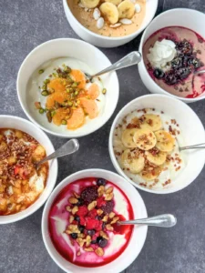 6 fully assembled yogurt bowls on a counter with spoons in the bowl.