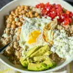 A fully assembled high protein savory Mediterranean-inspired bowl of oatmeal with avocado slices, tomatoes, chickpeas, cottage cheese, and a runny egg.