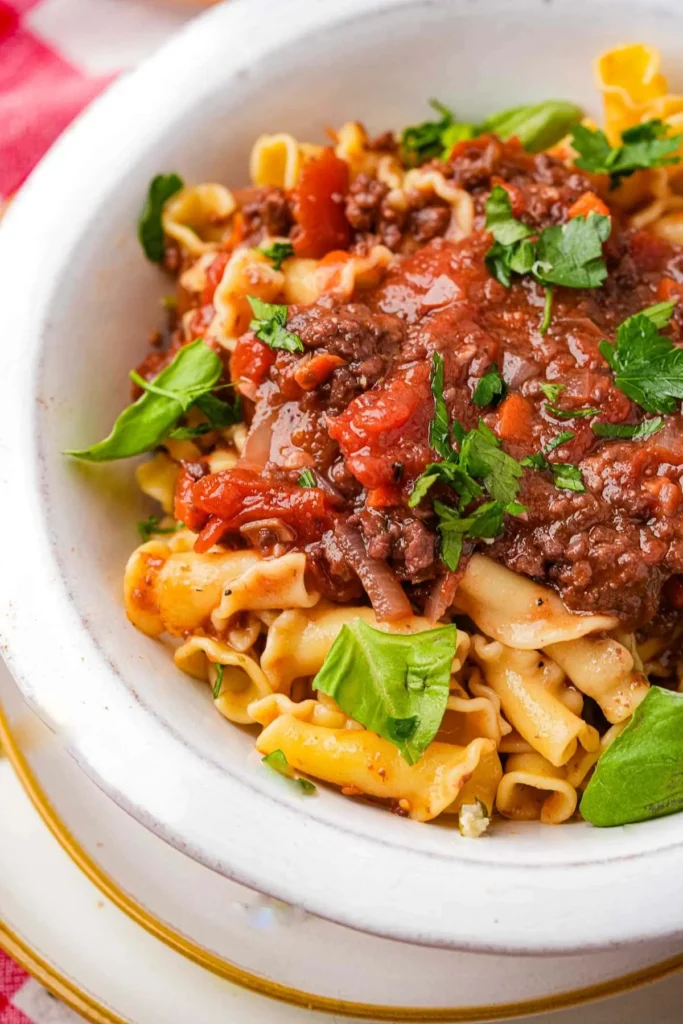 A bowl of pasta bolognese with seitan in a large white bowl.