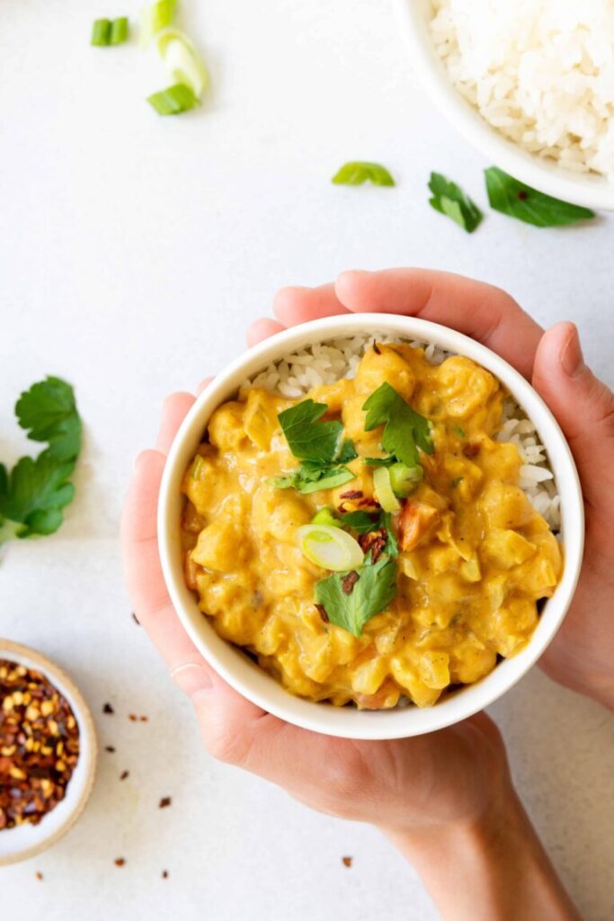 Someone holding a small bowl of chickpea coconut curry over a table.