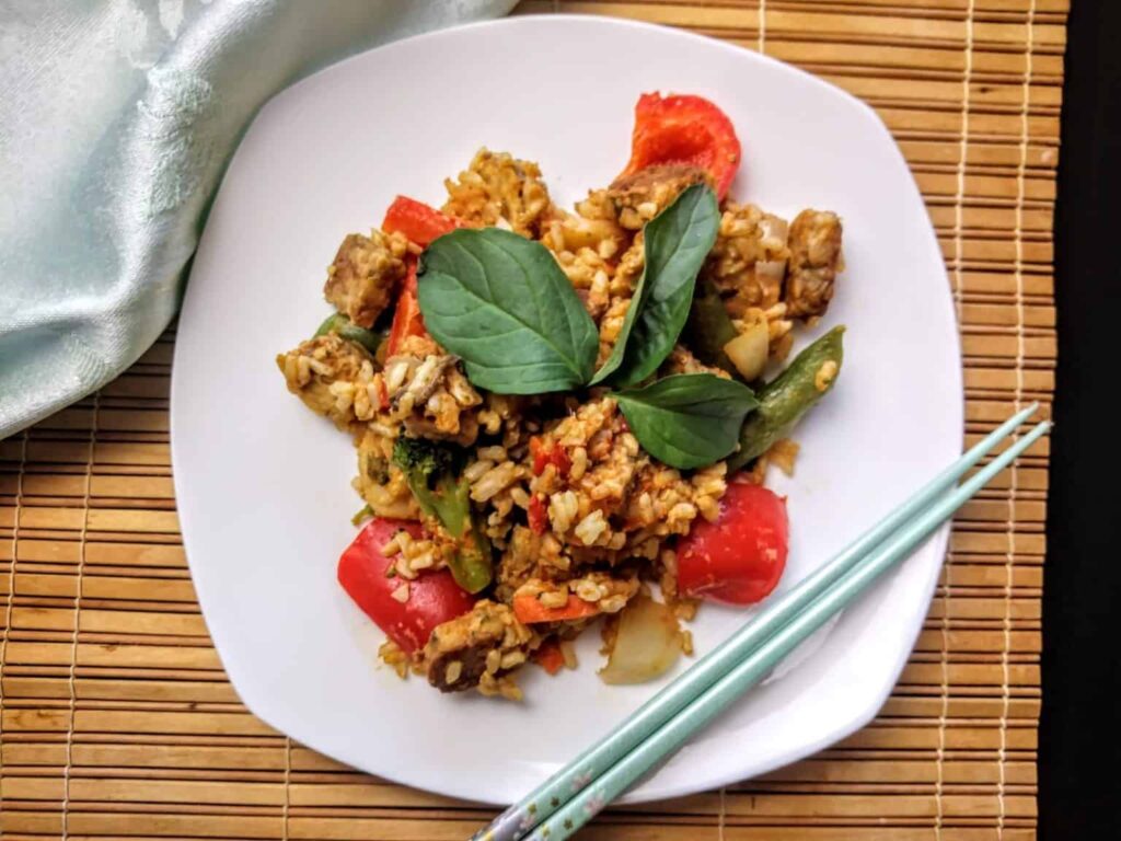 Thai peanut tempeh on a plate with chopsticks on a tablecloth on a table.