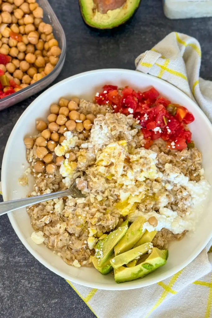 A birds-eye view of a Mediterranean diet oatmeal with the yolk dug into and mixed up with the oatmeal on a counter next to a bowl of chickpeas.