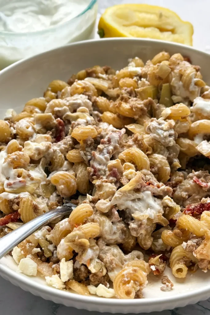 A bowl of pasta with the creamy yogurt and feta mixed into it on a table next to a lemon wedge.