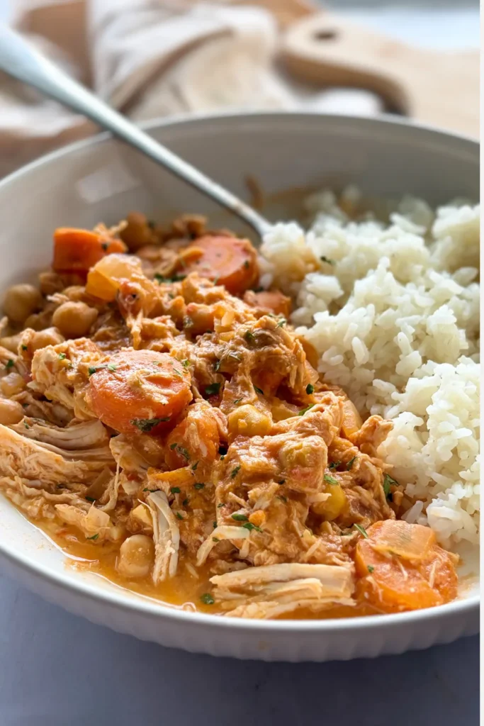 A close-up of a chicken, tomato, onion and carrots with rice with a fork on it.