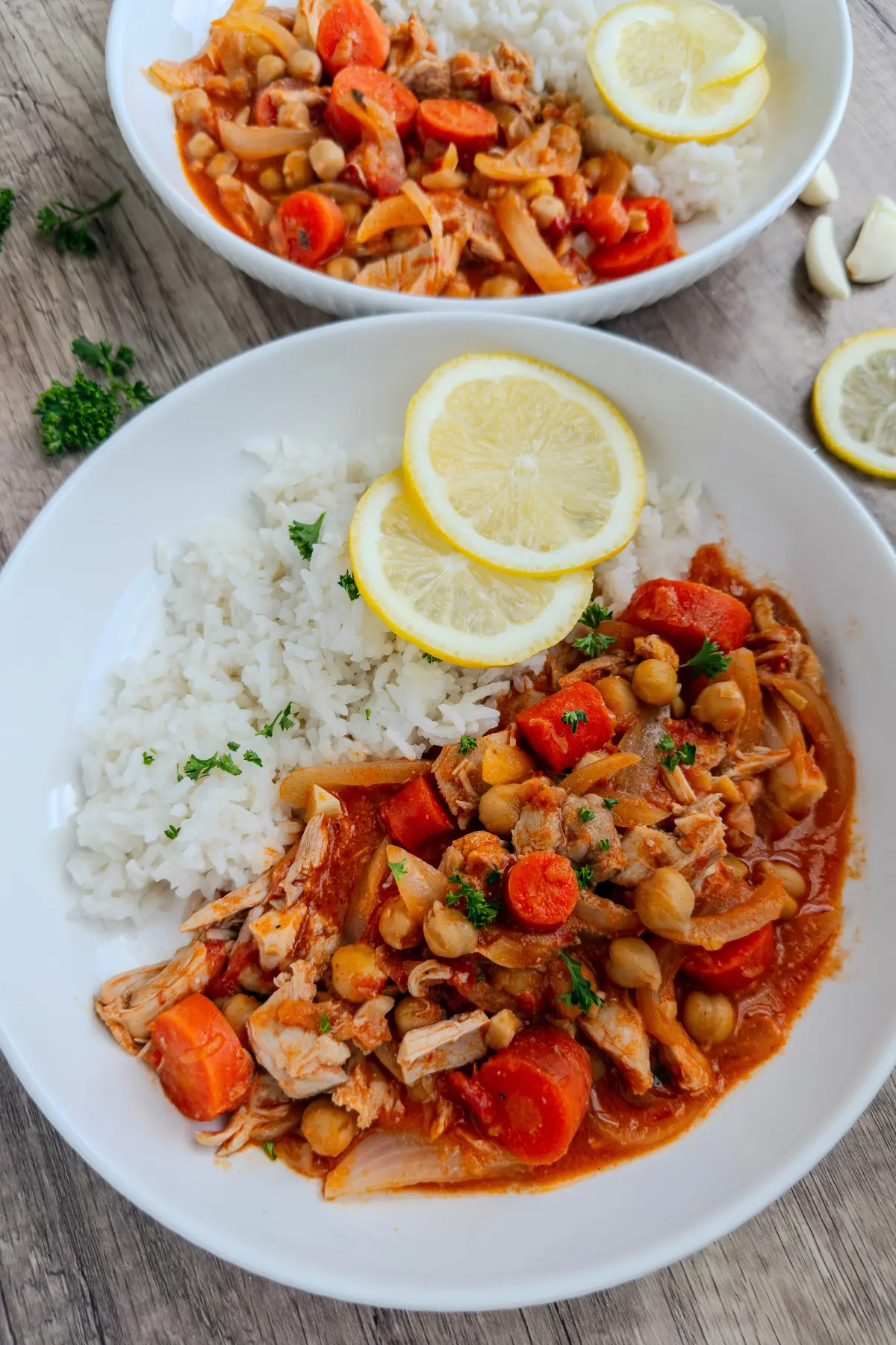 The crockpot coconut chicken with tomato sauce, carrots, chickpeas, and rice on two plates garnished with lemon wedges on a table.
