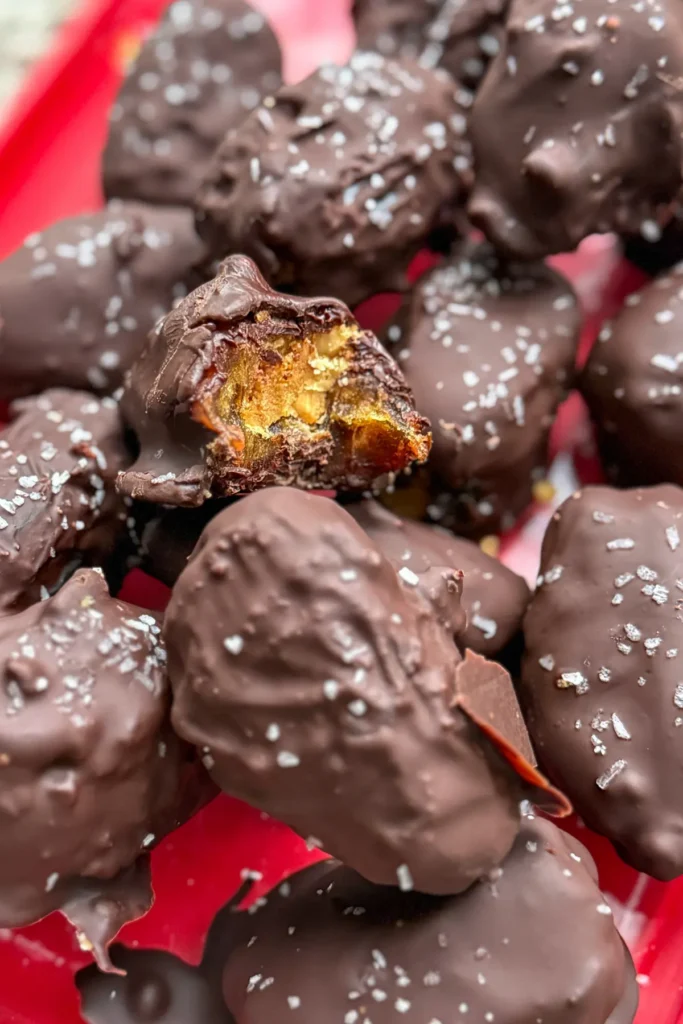 A storage container of dark chocolate dates with one half bitten on top.