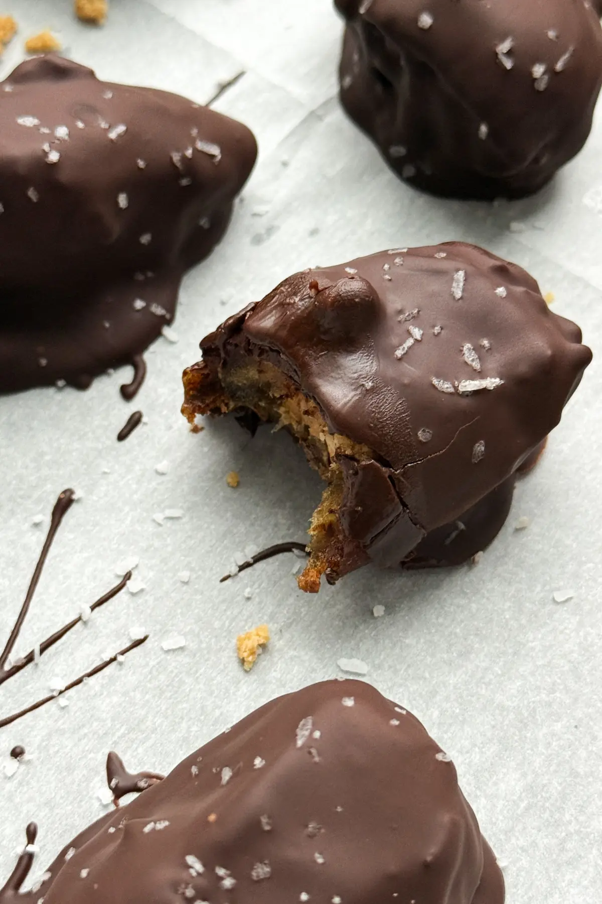A half bitten dark chocolate stuffed protein date on a sheet of parchment paper surrounded by more dates.