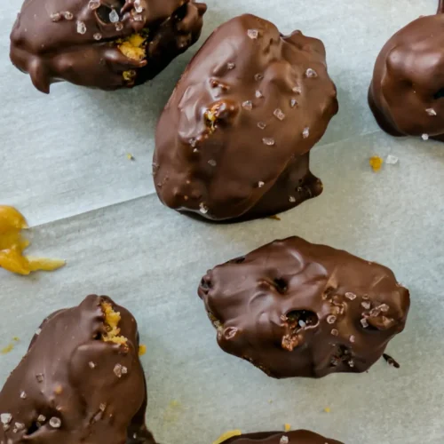 A birds-eye view of dark chocolate peanut butter stuffed dates with protein powder and sea salt on a baking sheet lined with parchment paper.