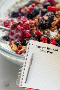 A pad of paper and a pen with the words 'improve you gut meal plan" with a chia breakfast bowl in the background on a counter.