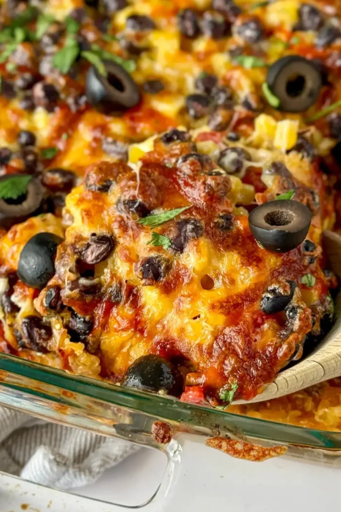 A close-up of a wooden spoon digging into a Mexican quinoa casserole in a baking dish.