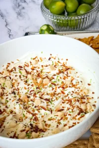 A large white bowl of key lime pie yogurt dip next to a bowl of key limes and a lime zester.