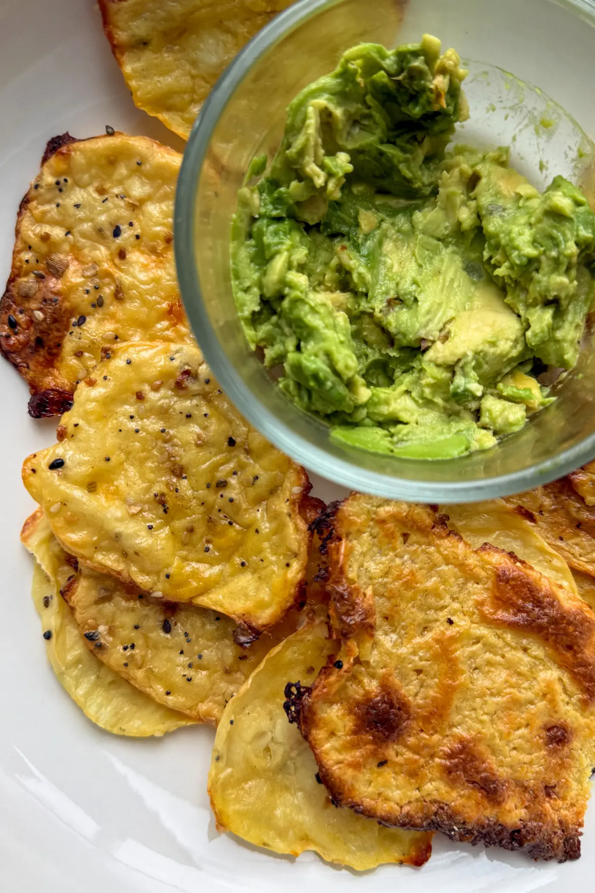 Cottage cheese crisps on a white plate with a bowl of guacamole in the middle.