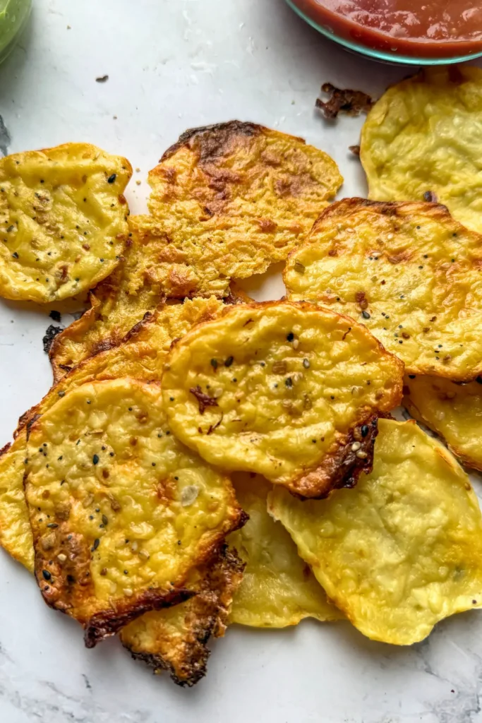 A pile of cottage cheese crisps on a counter next to a bowl of salsa.