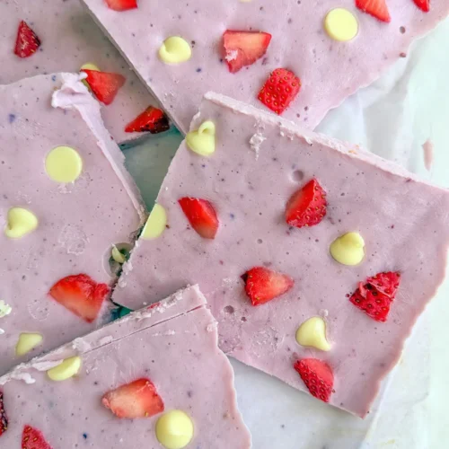Large slices of white chocolate and strawberry cottage cheese bark stacked on top of one another on parchment paper.