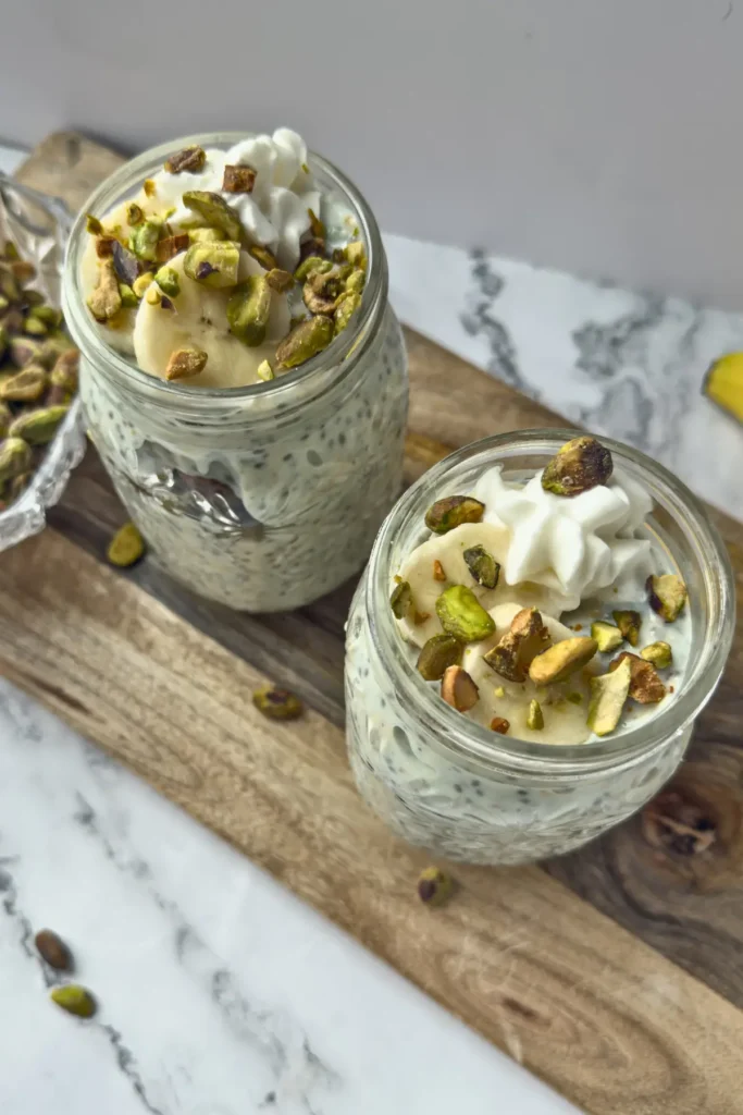 Two glass mason jars filled with pistachio pudding overnight oats with protein powder on a counter.