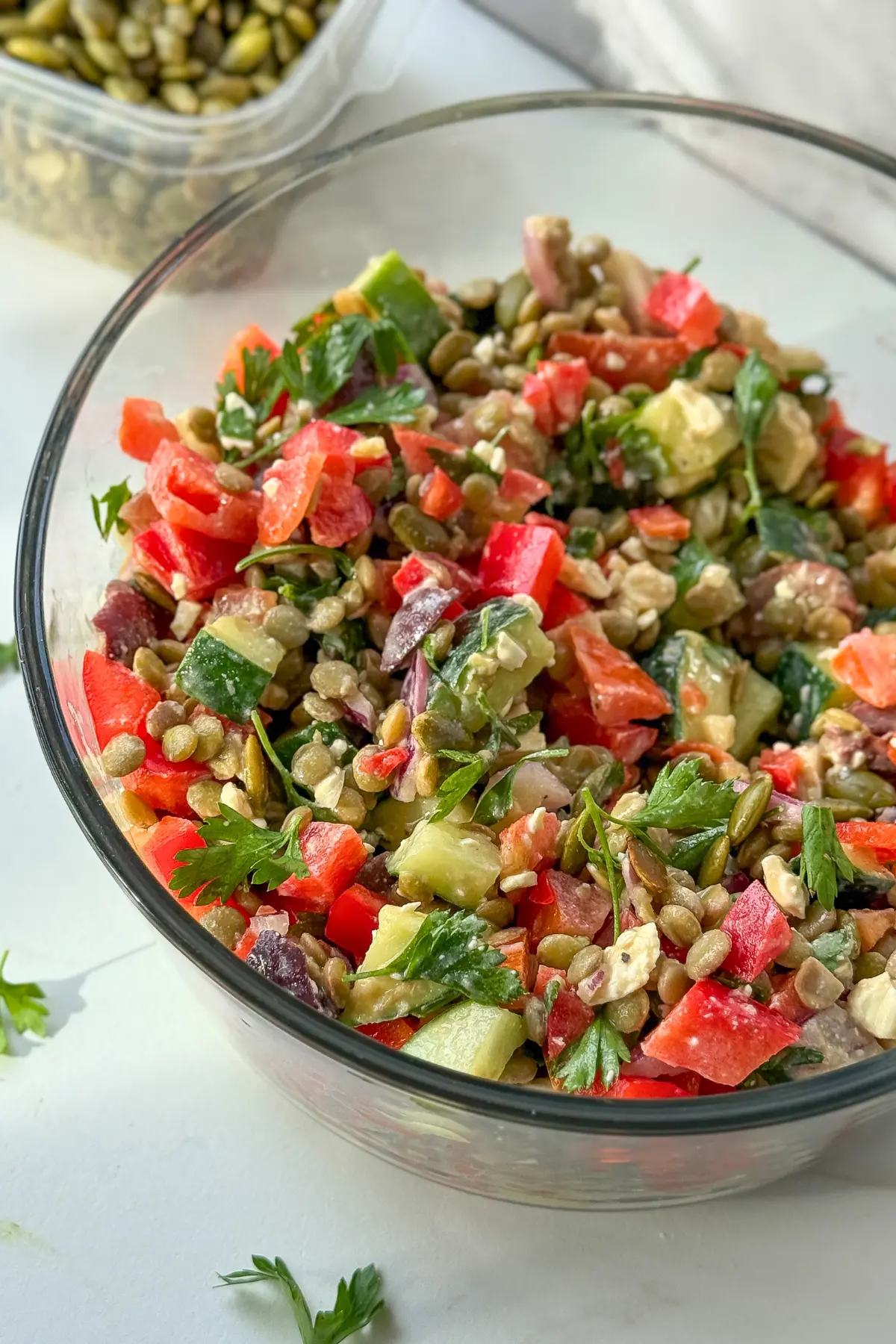 Fully assembled high protein lentil salad with nooch dressing in a glass bowl on a counter next to a bowl of salted pepitas.
