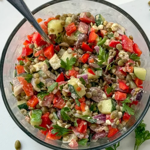A birds-eye view of high protein lentil salad in a glass bowl with a fork in it on a counter.