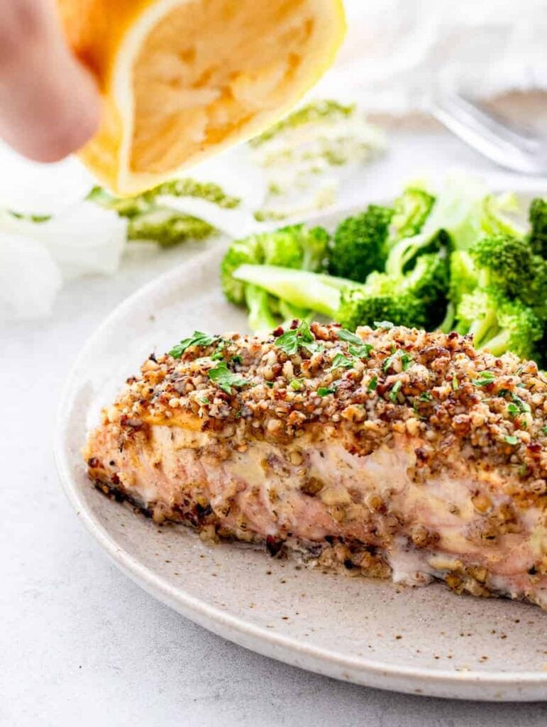 Walnut crusted salmon on a plate next to broccoli on a table.
