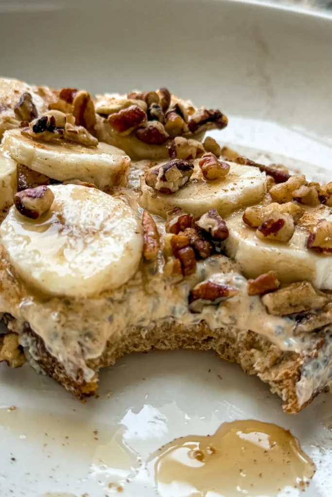 A close-up of cottage cheese pumpkin toast with banana slices and pecans with a bite taken out of it on a white decorative plate.