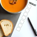A pot of pumpkin soup on a counter next to a checklist and a pen and slices of bread.