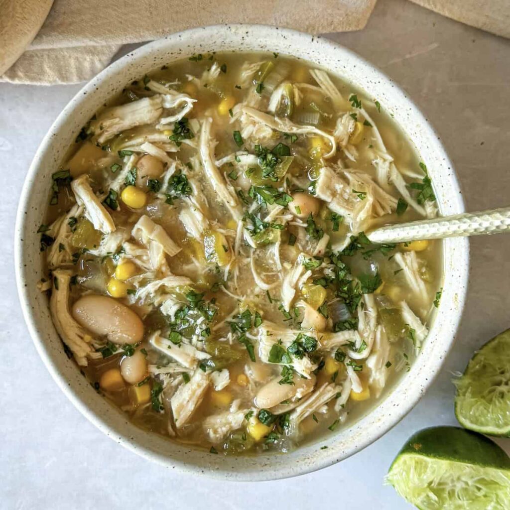 A birds-eye view of a bowl of white chicken chili wth a spoon in it on a table.