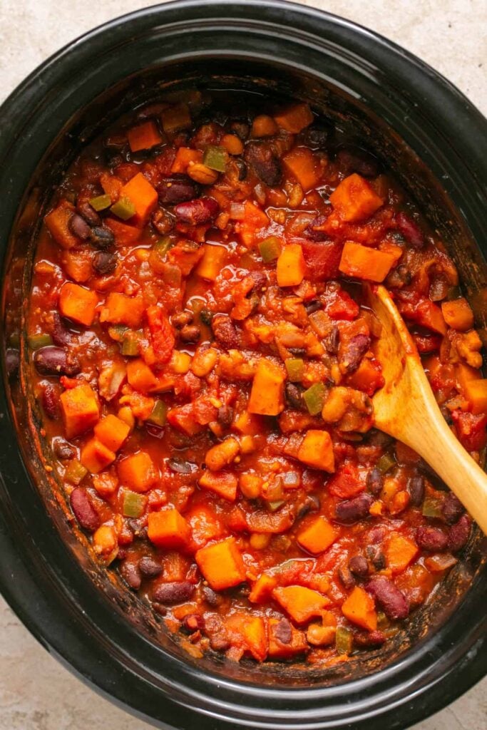 A birds-eye view of sweet potato chili in a slow cooker with a wooden spoon.