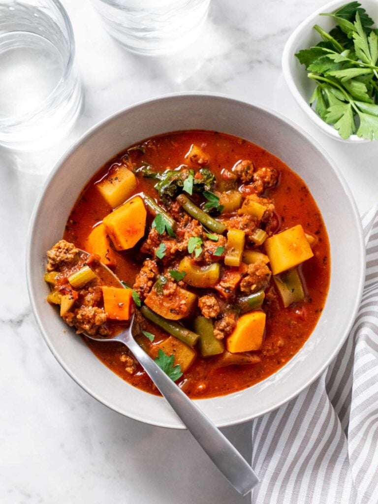 A birds-eye view of a bowl of hamburger soup with a spoon in it on a table.