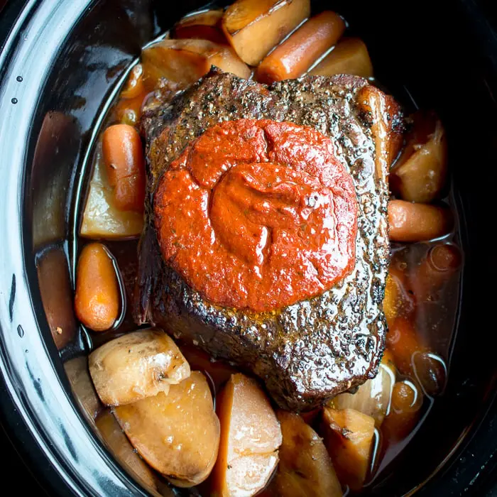 An large beef round on top of potatoes and carrots in a slow cooker.
