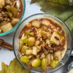 A birds-eye view of two fully assembled yogurt bowl topped with a cooked pear and pecan mixture.