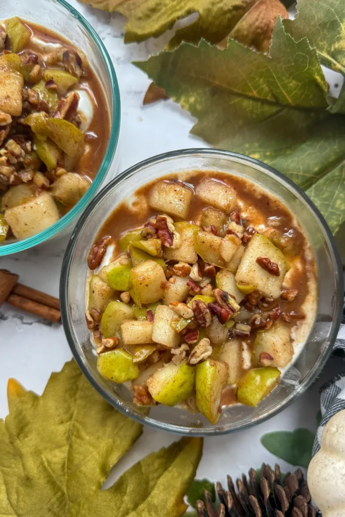 A birds-eye view of two fully assembled yogurt bowl topped with a cooked pear and pecan mixture.