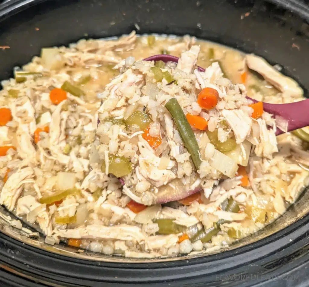 A slow cooker with fully cooked chicken barley soup.