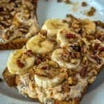 A slice of toast topped with sliced banana, whipped pumpkin and cottage cheese, chopped pecans, and a drizzle of maple syrup on a white plate.