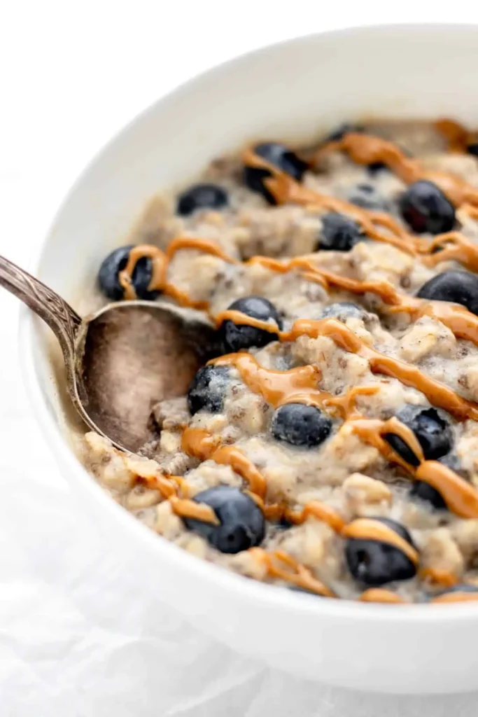 A close-up of a macro-friendly bowl of oatmeal with drizzled peanut butter and blueberries.