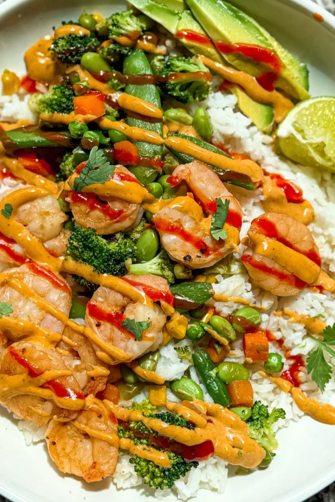 A birds-eye view of shrimp, rice, and mixed vegetables in a bowl with sauces drizzled over it.