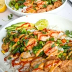 Two fully assembled macro-friendly shrimp and rice bowls on a counter next to half an avocado, half a lime, and different sauces.