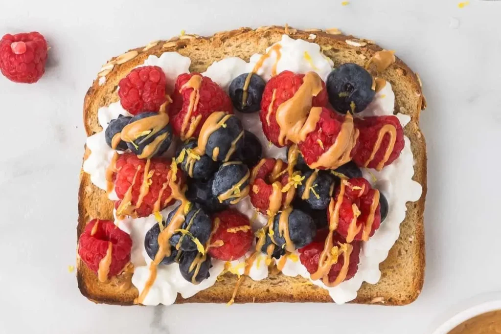A slice of bread with cottage cheese, berries, and drizzled peanut butter on it.
