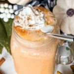 A pumpkin and vanilla pudding protein shake topped with whipped cream with a straw in it on a counter.