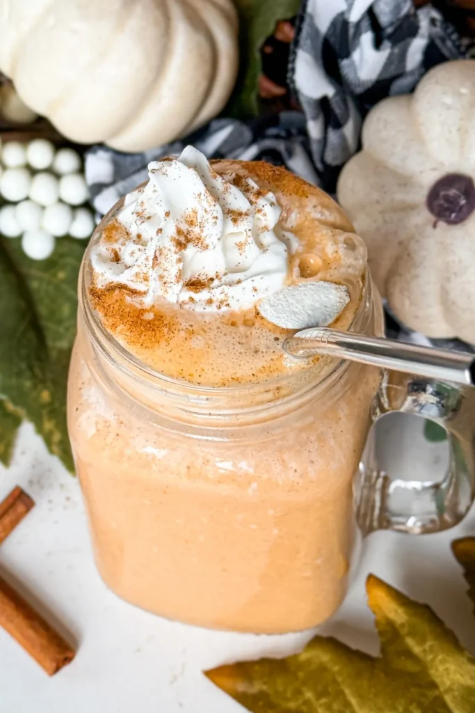 A pumpkin and vanilla pudding protein shake topped with whipped cream with a straw in it on a counter.