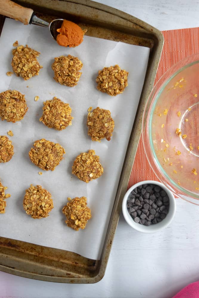 Pumpkin no bake cookies spread out on parchment paper on a cookie sheet on a counter.