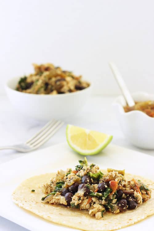 A tofu and black bean open-faced wrap on a counter next to a fork and a bowl of the tofu scramble.