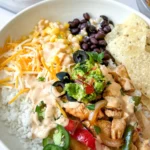 A fully assembled chicken fajita bowl served over rice with shredded cheese, guacamole and jalapenos in a bowl on a counter next to a bowl of guacamole.