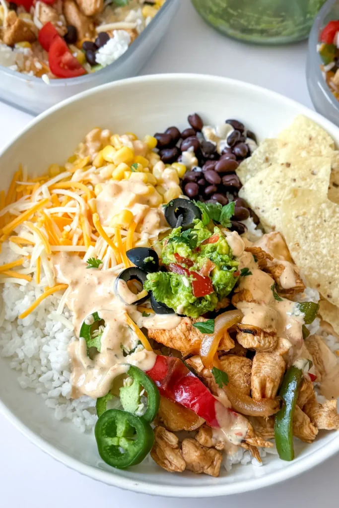 A fully assembled chicken fajita bowl served over rice with shredded cheese, guacamole and jalapenos in a bowl on a counter next to a bowl of guacamole.