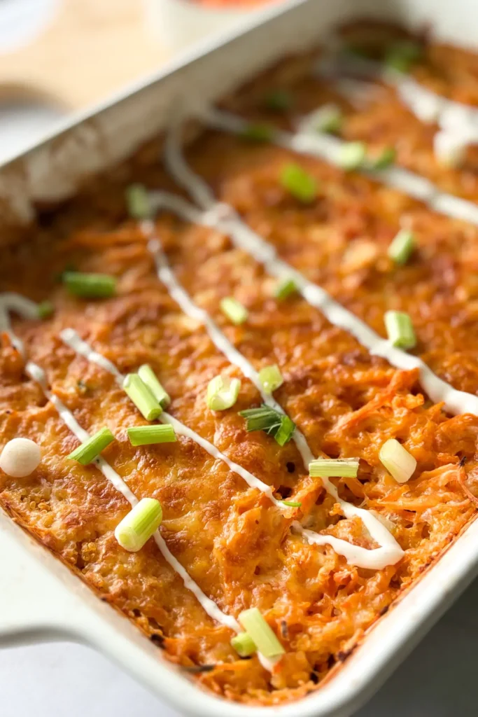 A shot of the buffalo chicken casserole in a white 9 x 13 dish with the crispy cheese topping and ranch dressing drizzle.