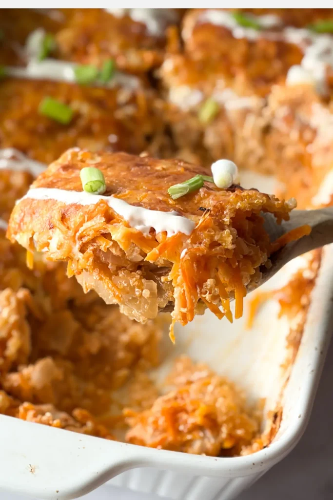 A big slice of buffalo chicken quinoa on a wooden spoon being held over the casserole dish.