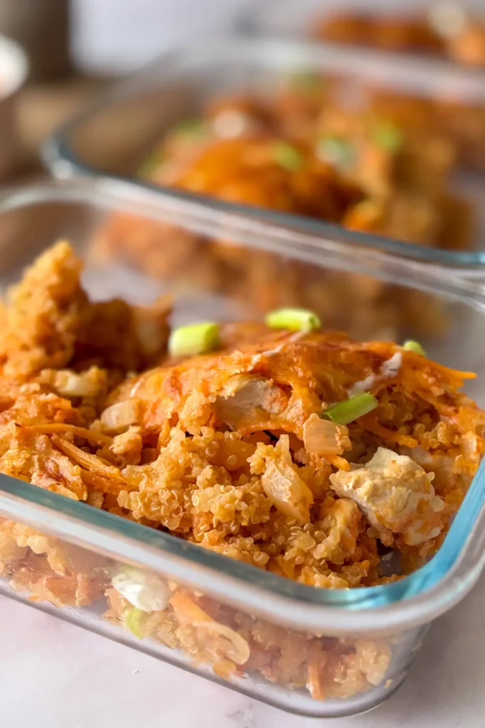 Buffalo chicken and quinoa portioned out into meal prep containers on a counter.