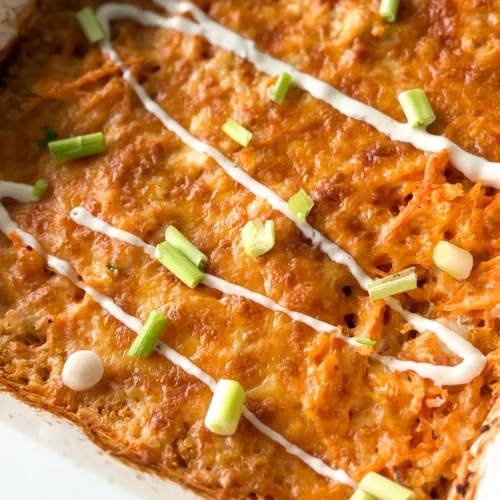 A close-up of the buffalo chicken quinoa casserole in a white casserole dish drizzled with ranch dressing and topped with green onions.