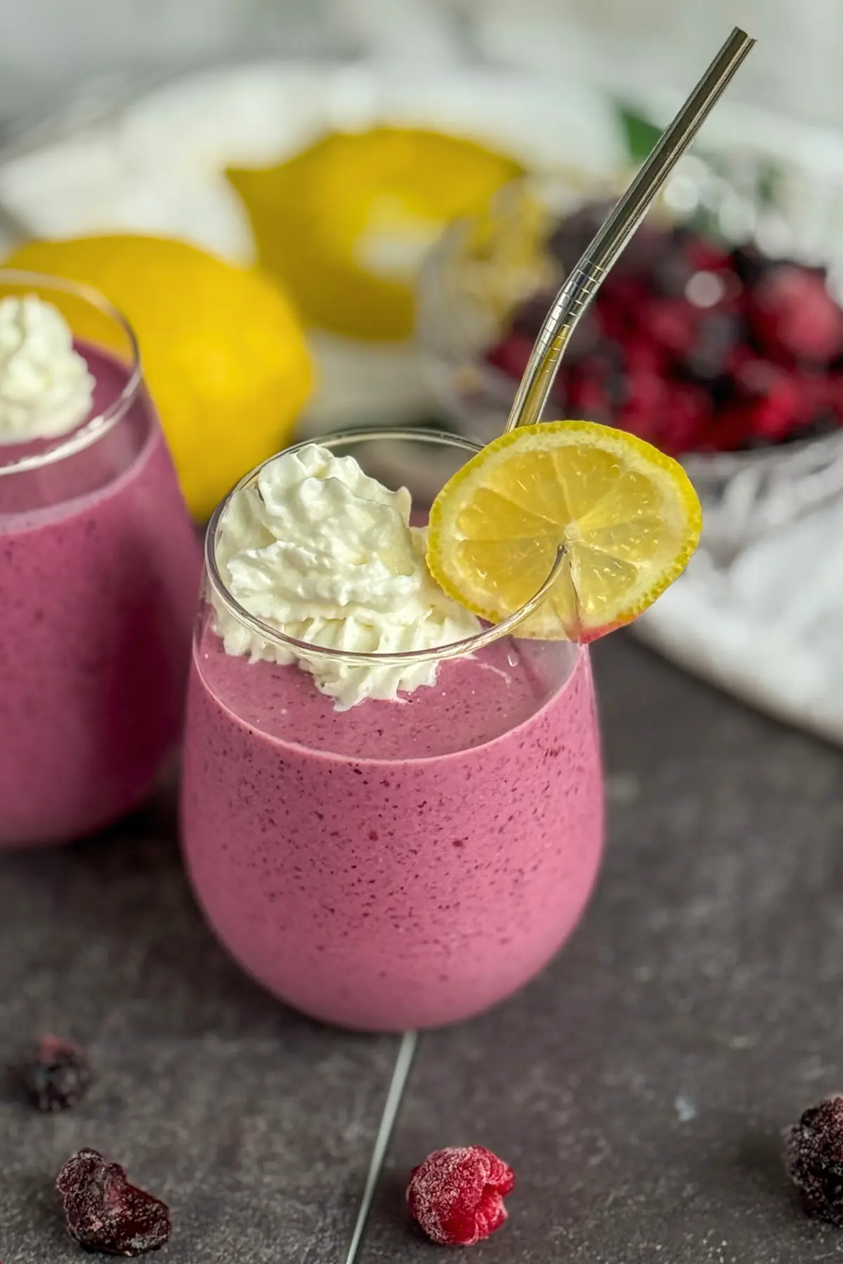 A lemon berry smoothie garnished with lemon wedges and whipped cream on a counter with lemons in the background.